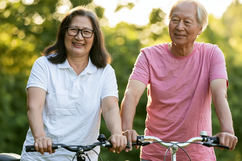 Senior asian couple smiling while cycling together in a sunlit park