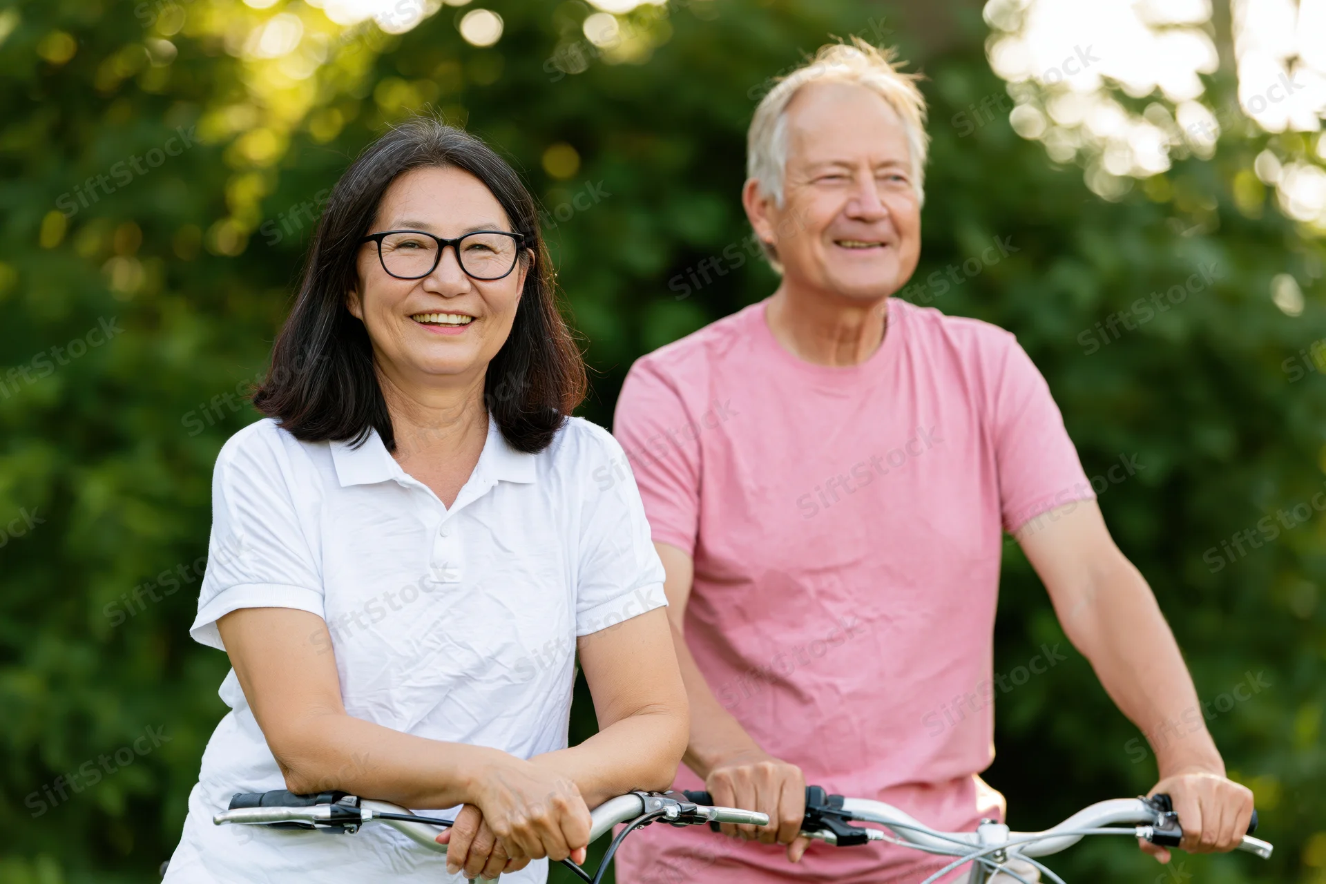 Smiling senior couple cycling together in a green park on a sunny day