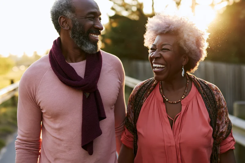 Older african couple laughing and walking together outdoors at sunset