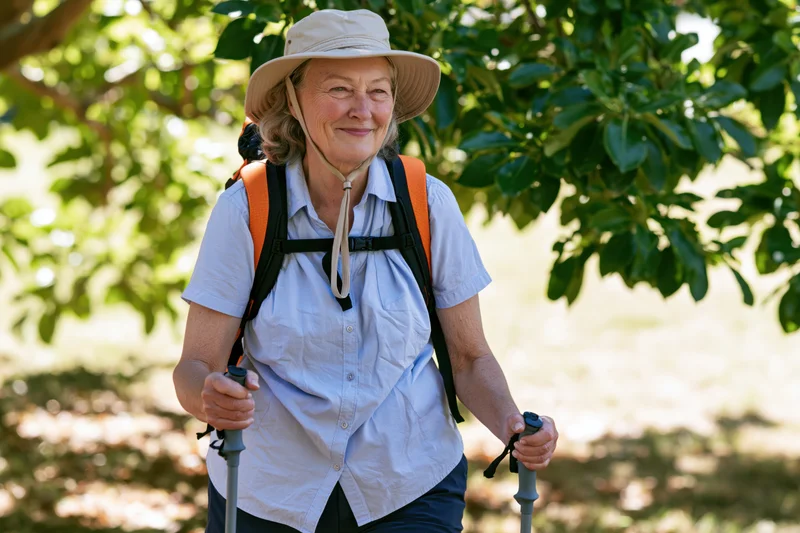 Senior woman hiking with backpack and trekking poles on a sunlit forest trail