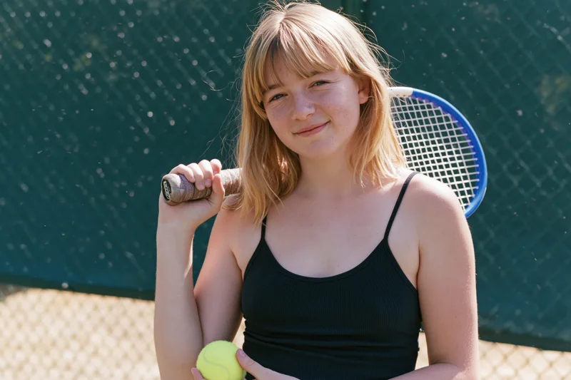 Young woman holding tennis racket and ball, smiling on outdoor court