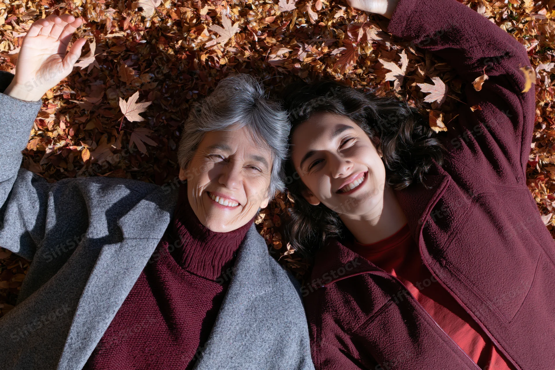 Two women lying on autumn leaves smiling at camera from above