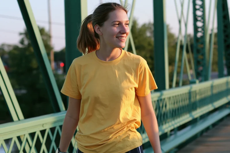 Young woman smiling while walking on a green metal truss bridge outdoors