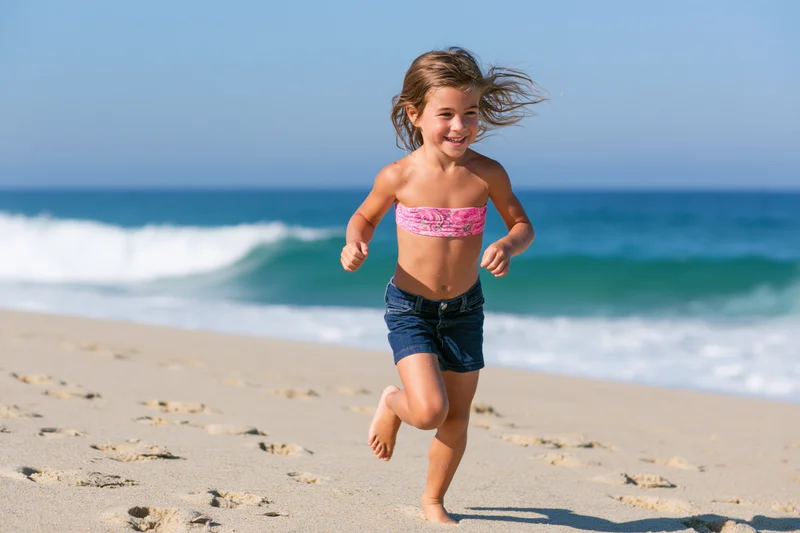 Young girl running barefoot on sandy beach with ocean waves in background