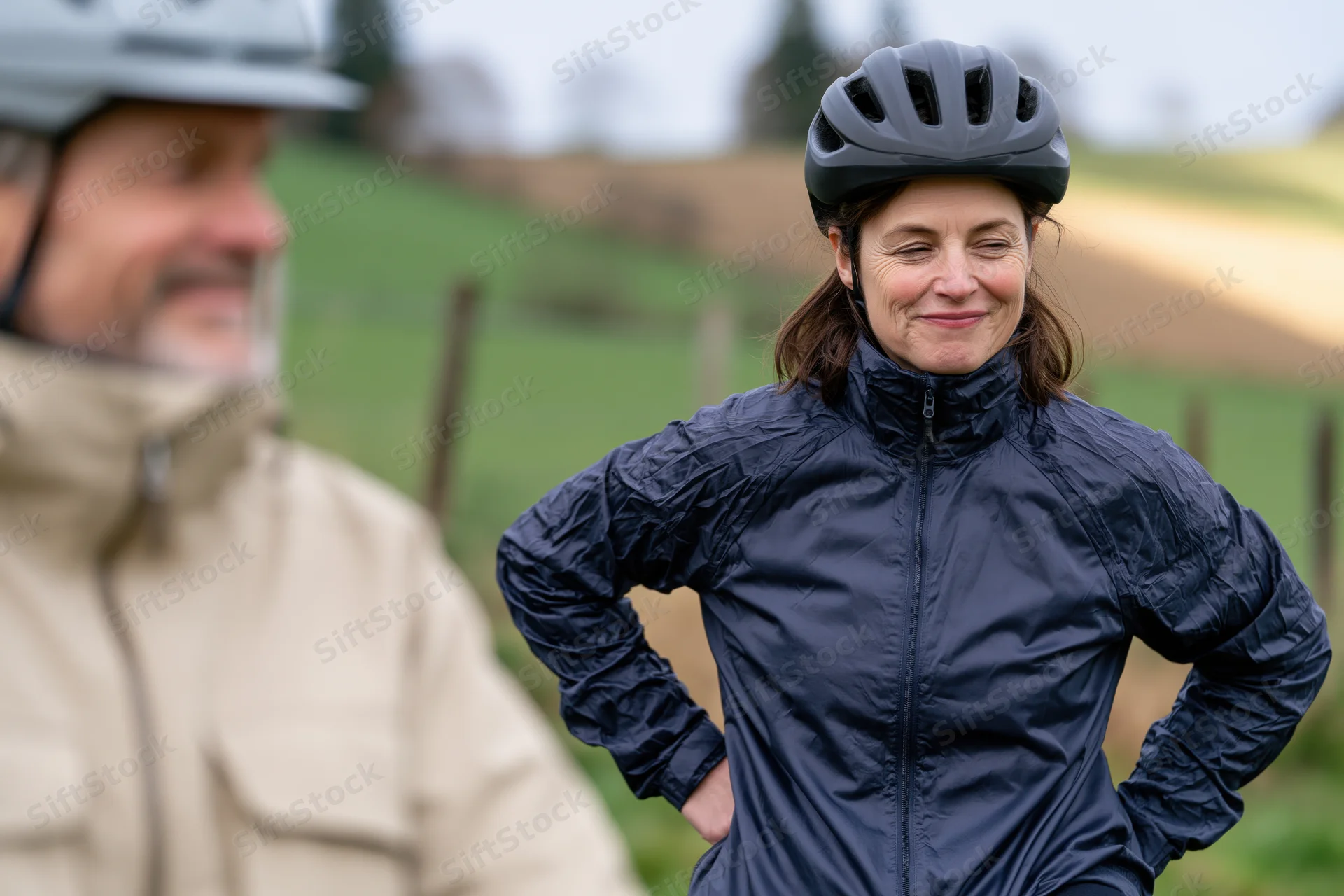 Woman cyclist smiling with hands on hips during outdoor bike ride in rural field