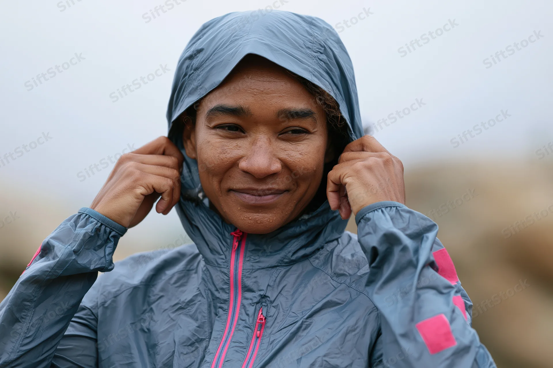 Woman adjusting hood on gray waterproof jacket outdoors smiling