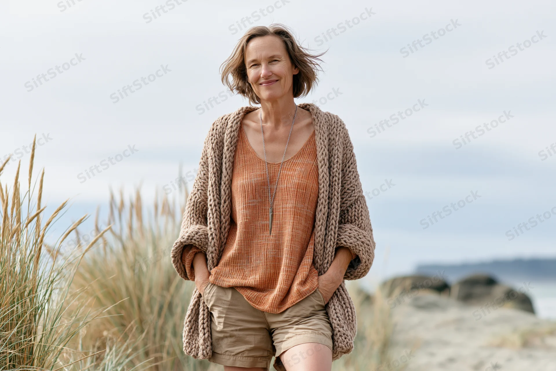 Woman smiling with hands in pockets on a windy beach near dunes and sea