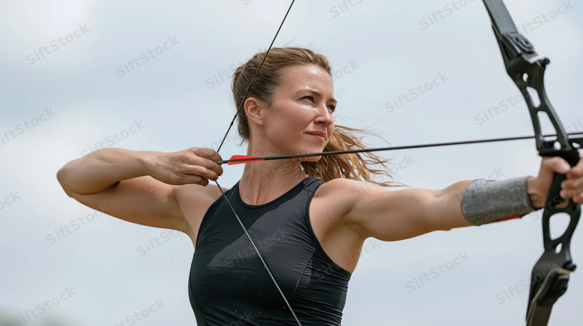 Woman aiming bow and arrow outdoors in athletic stance