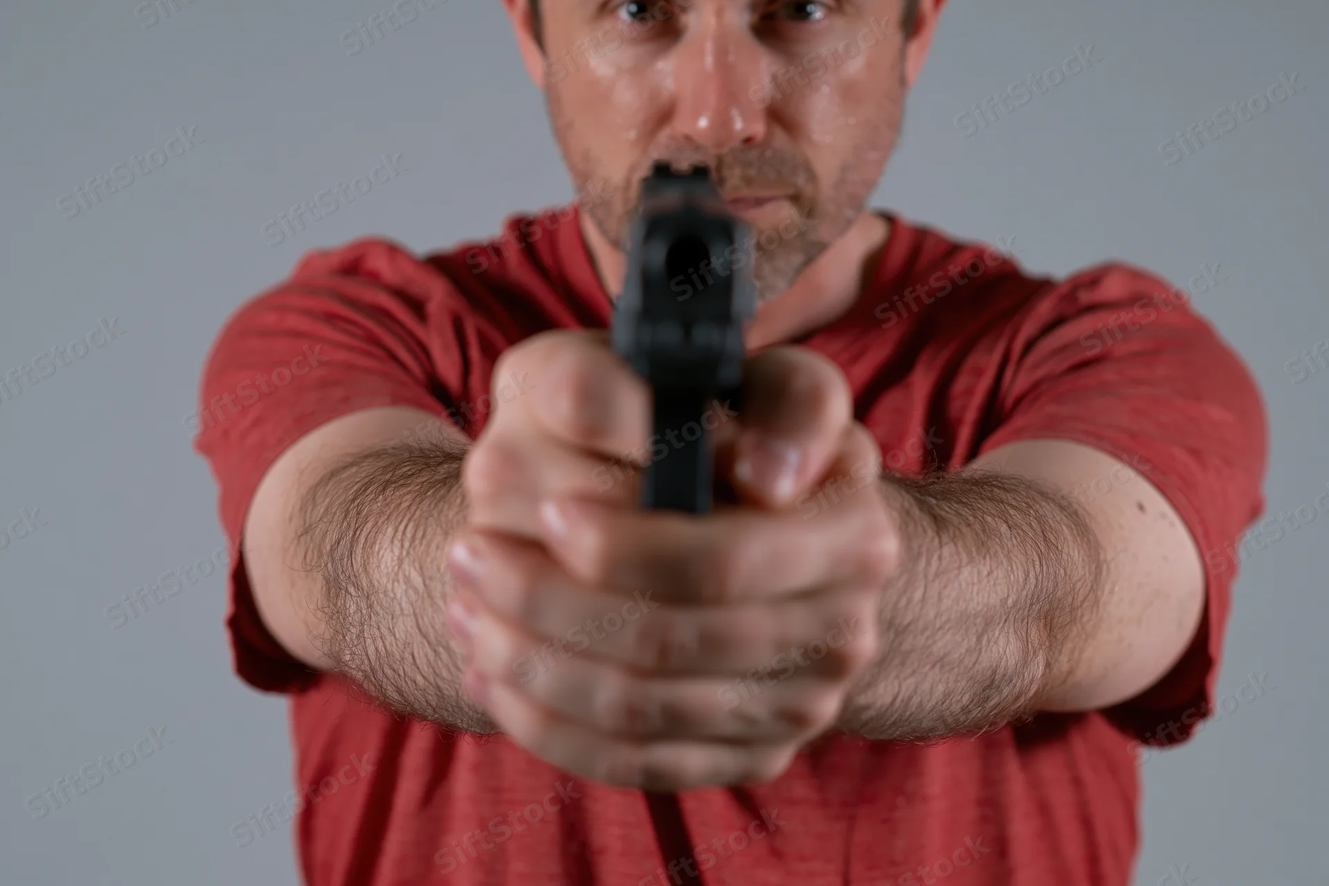 Man aiming handgun with two-handed grip in studio portrait