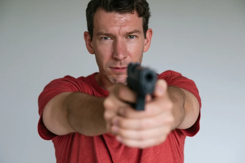 Man aiming handgun with both hands in studio setting