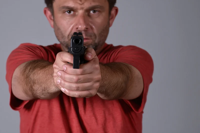 Man aiming handgun with two-handed grip in studio setting
