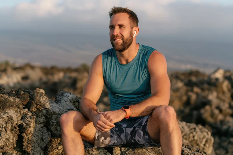 Man sitting on volcanic rock outdoors wearing fitness gear and earbuds during golden hour