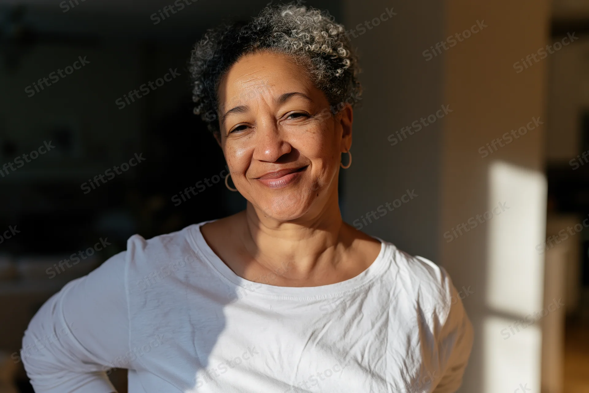 Middle-aged black woman smiling in natural sunlight indoors wearing white tshirt