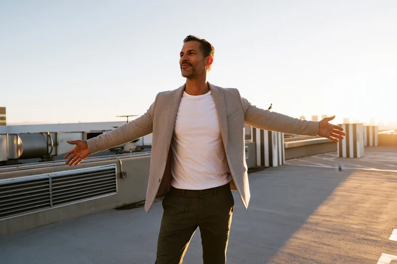 Man standing on rooftop with arms open at sunset