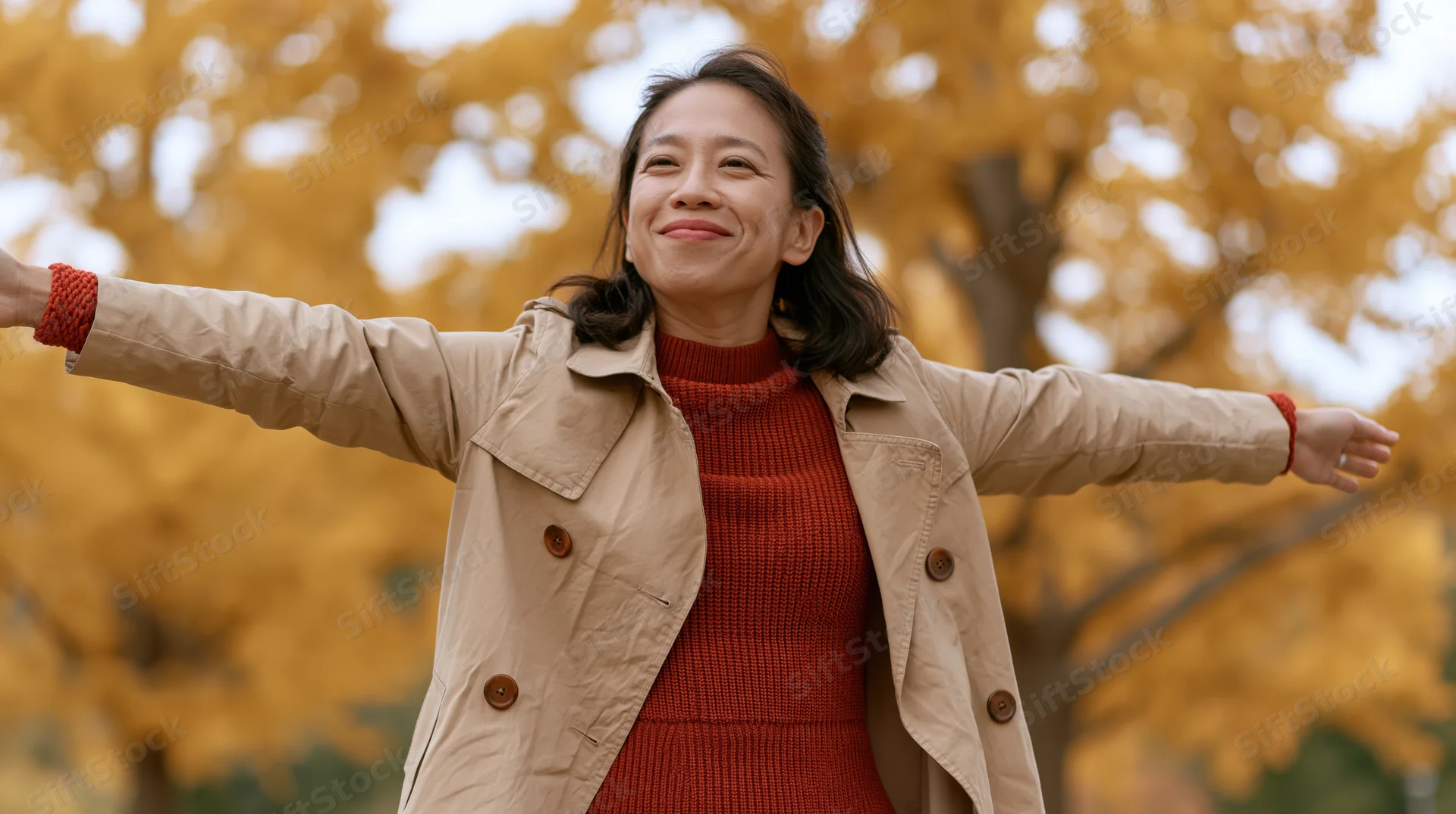 Woman smiling with arms outstretched in a park surrounded by yellow autumn trees