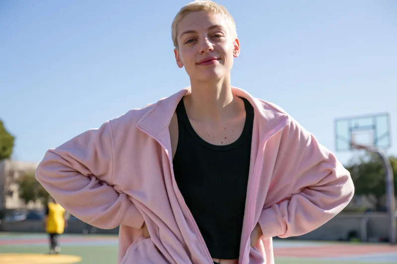 Woman with short blonde hair smiling in pink hoodie on basketball court