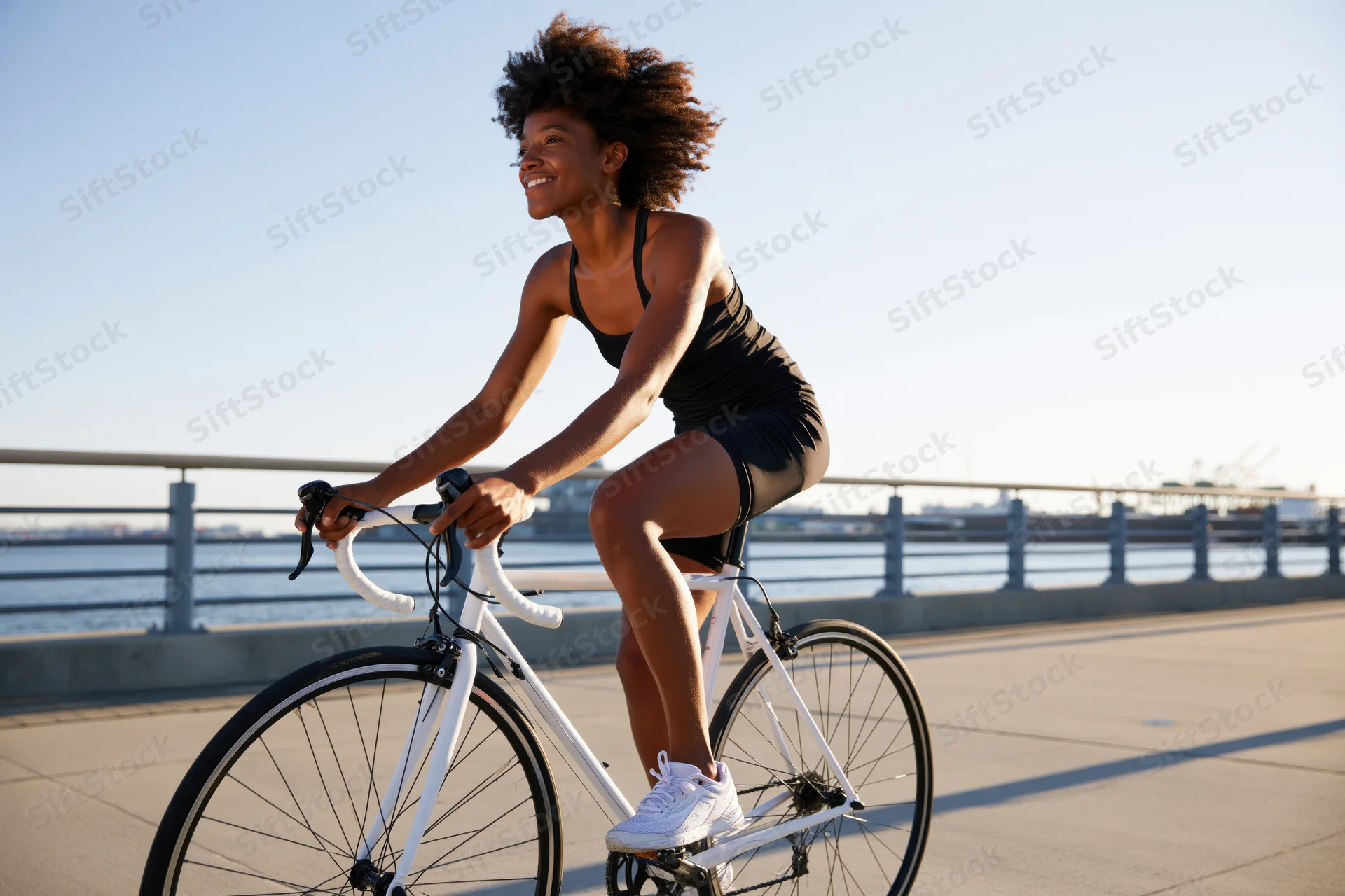 Young black woman cycling on a waterfront bridge in daylight