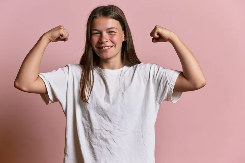 Young girl flexing both arms and smiling in front of pink background