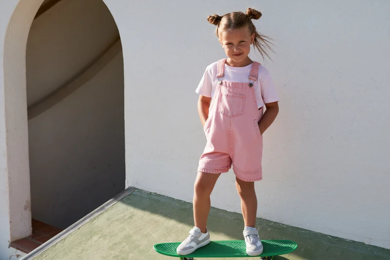 Young girl standing confidently on a green skateboard in front of a white wall with an arched doorway