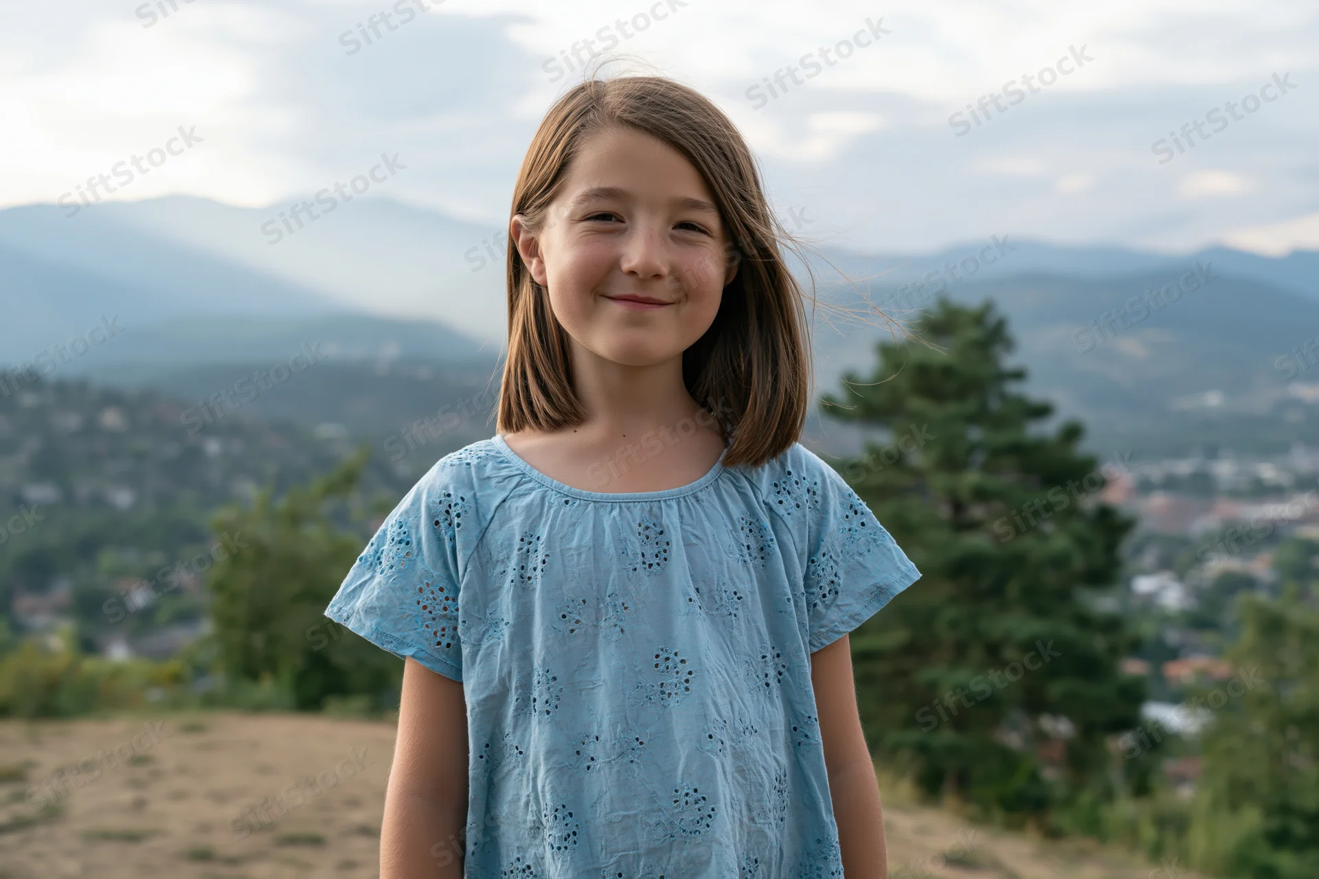 Young girl smiling outdoors on a hill with mountains and trees in the background