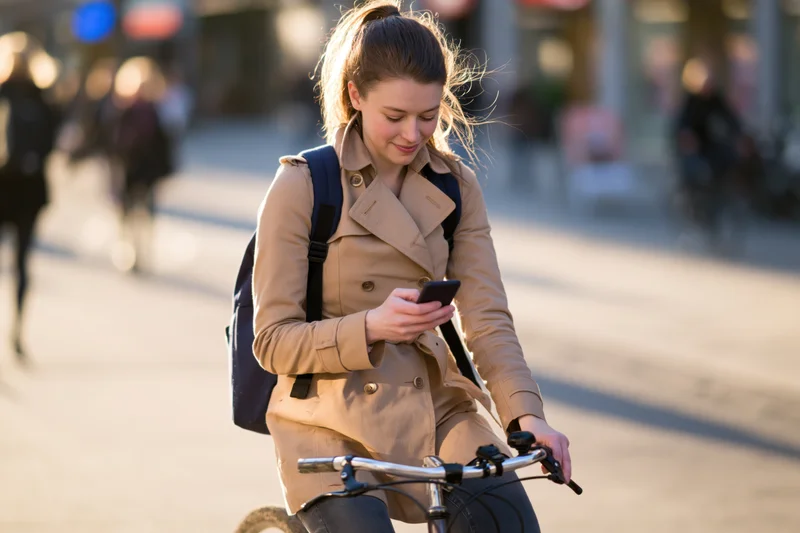 Young woman riding bicycle while using smartphone on city street