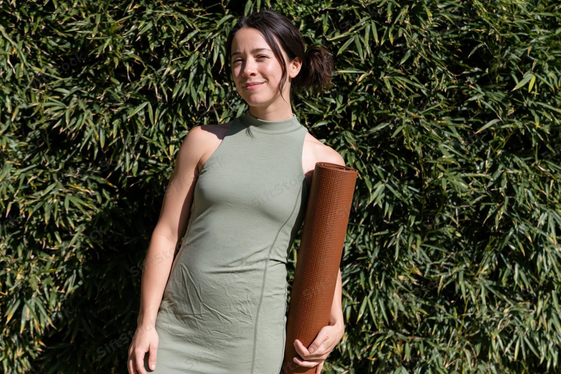 Young woman holding a yoga mat outdoors in front of bamboo foliage