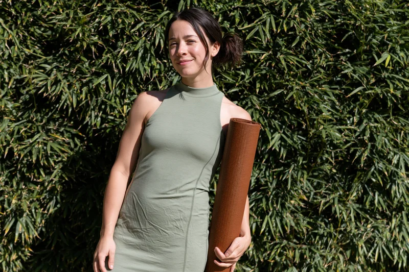 Young woman holding a yoga mat outdoors in front of bamboo foliage