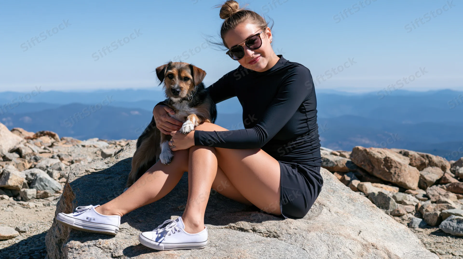 Young woman sitting on a rock with her dog at a mountain summit, overlooking a scenic landscape