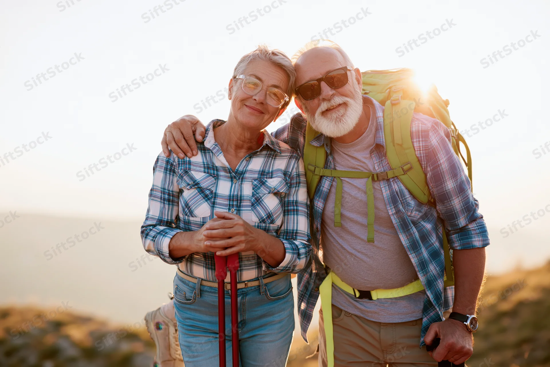 Senior couple hiking outdoors with backpack and trekking poles at sunset