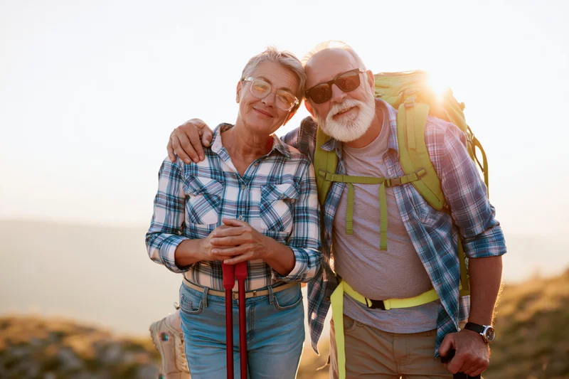 Senior couple hiking outdoors with backpack and trekking poles at sunset