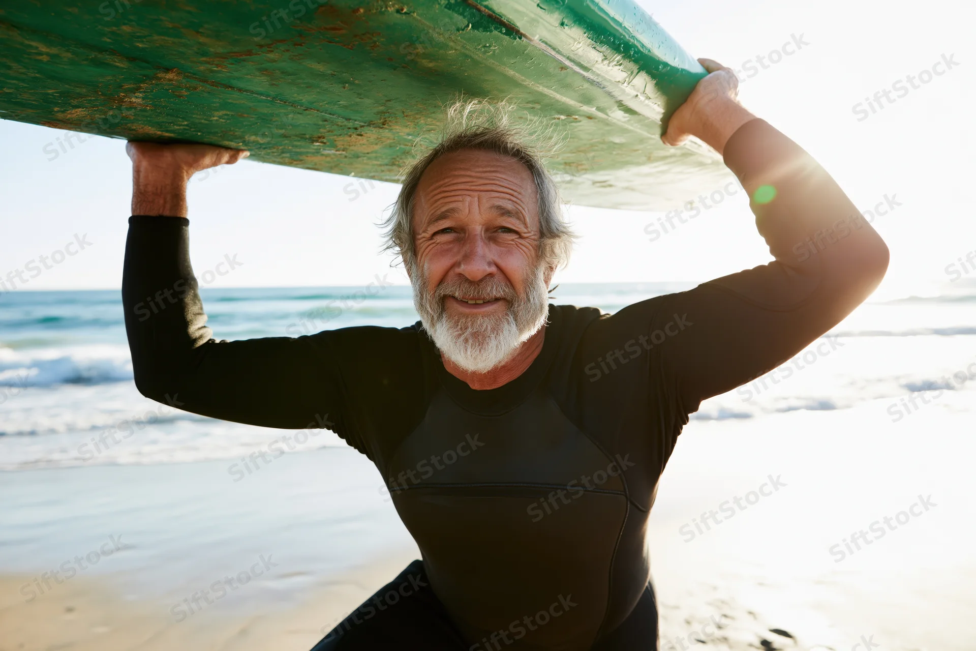 Senior man smiling while carrying surfboard on beach near ocean