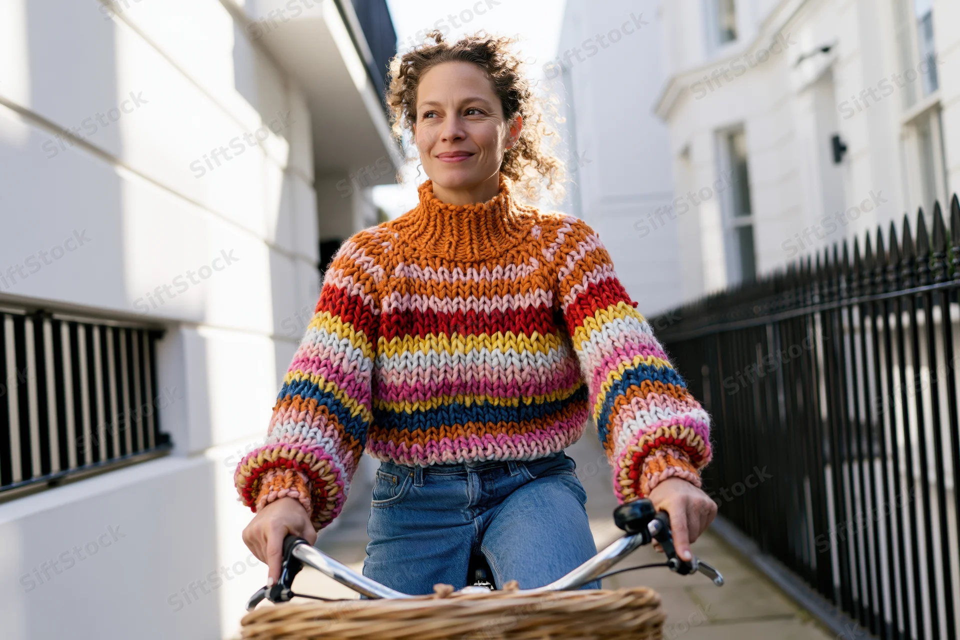 Woman riding bicycle on city sidewalk wearing colorful knitted sweater