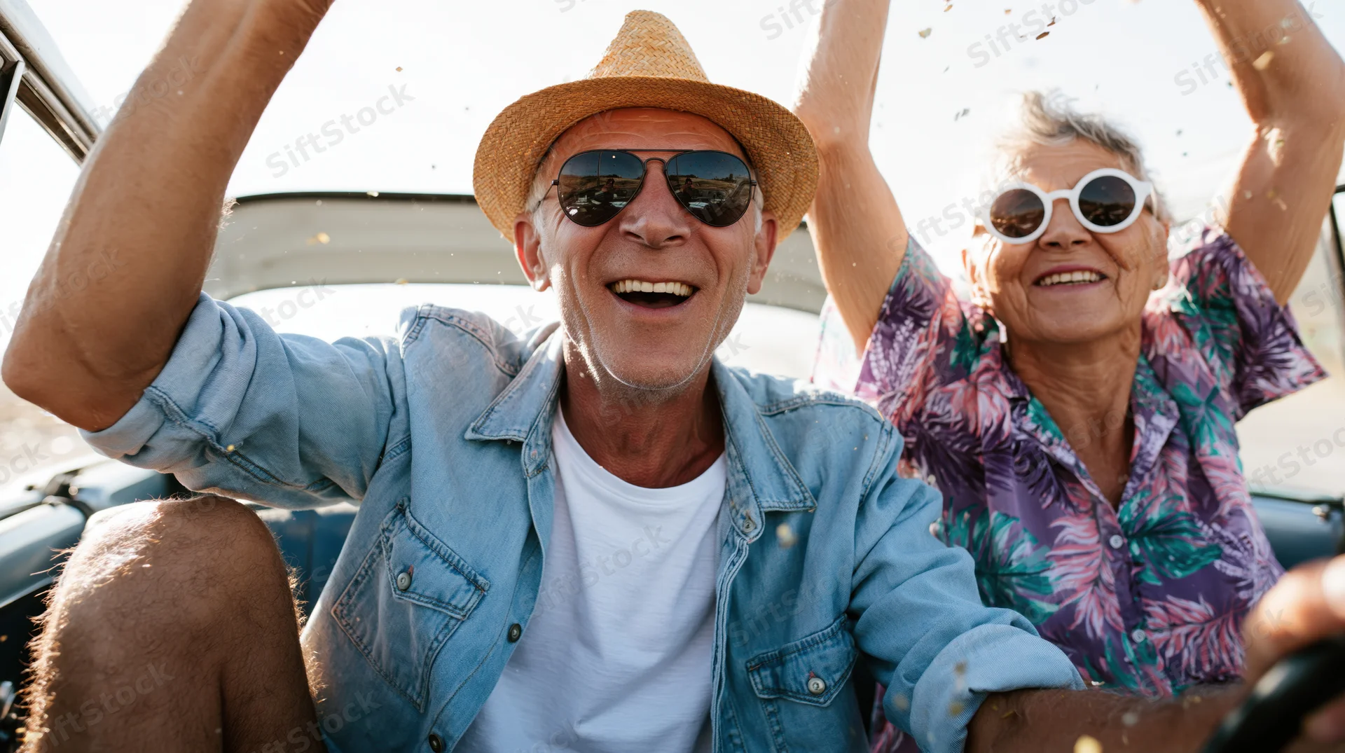 Senior couple smiling with arms raised while driving in a vintage convertible car