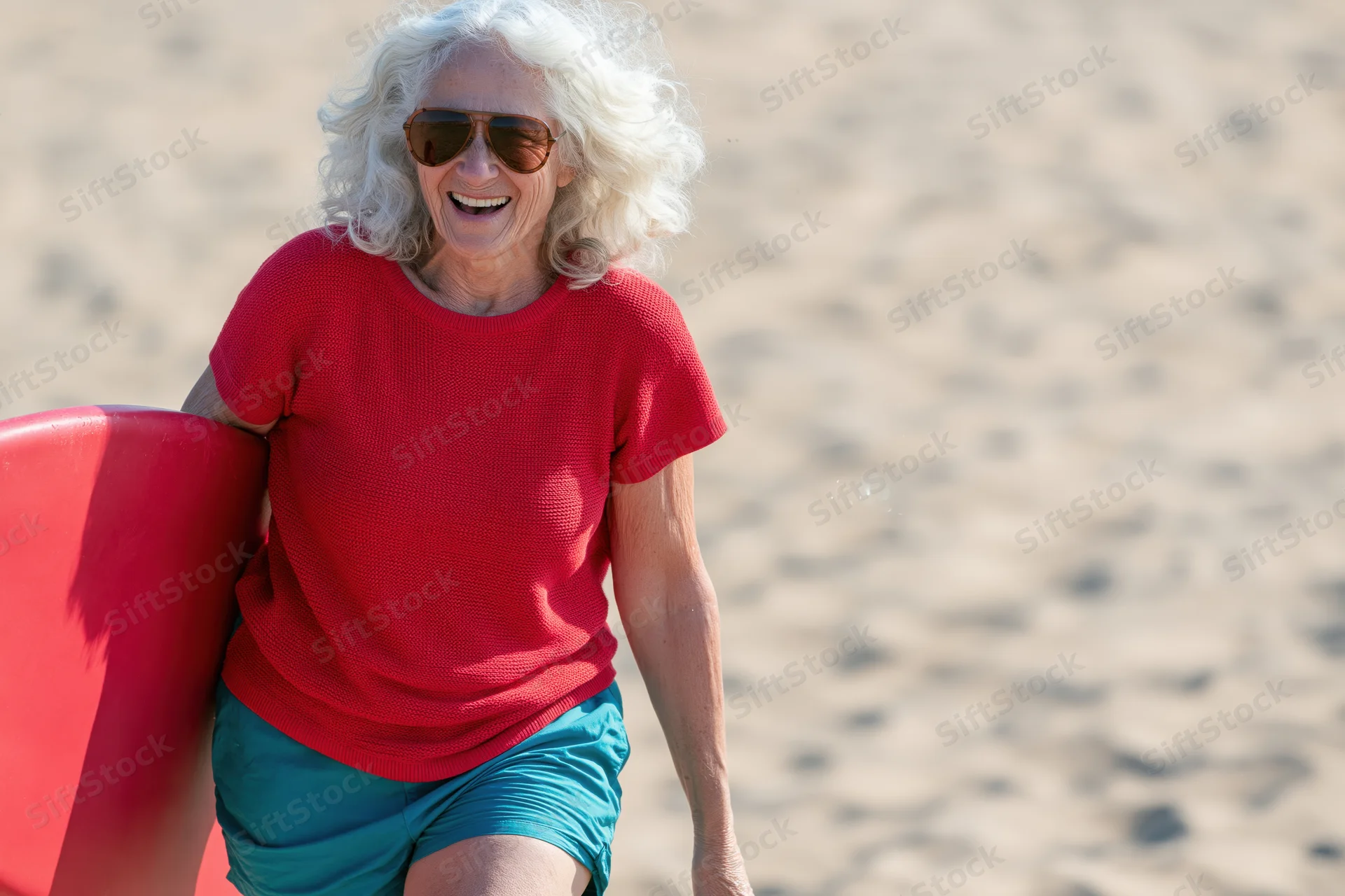 Senior woman smiling while carrying a red surfboard on a sandy beach