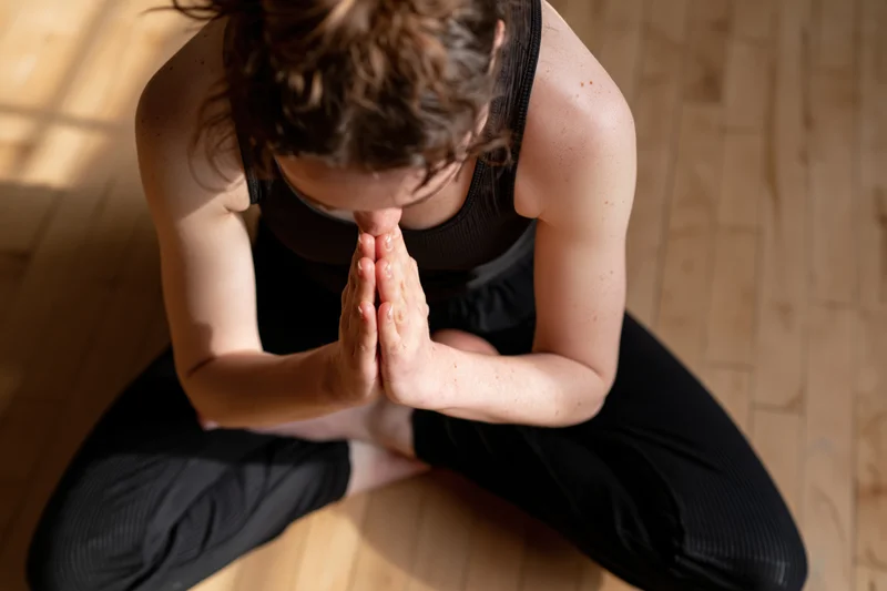 Woman in seated yoga pose with hands pressed together on wooden floor