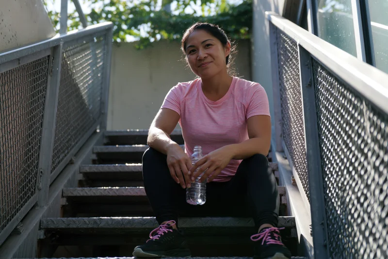 Woman sitting on outdoor metal staircase holding water bottle after exercise