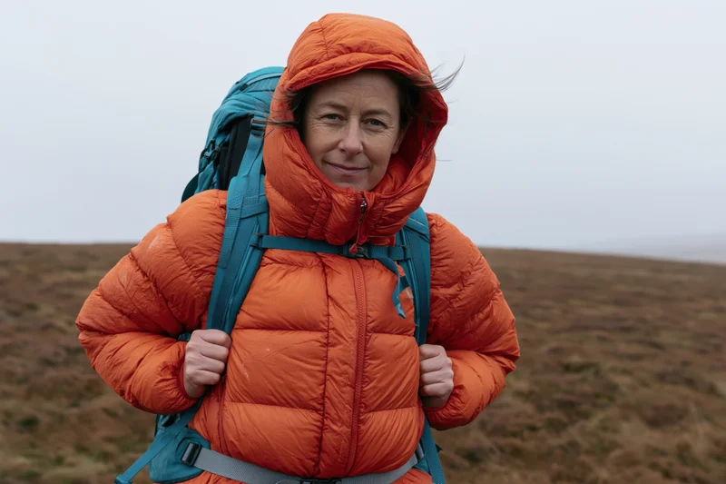 Woman hiking in orange jacket with blue backpack on moorland trail