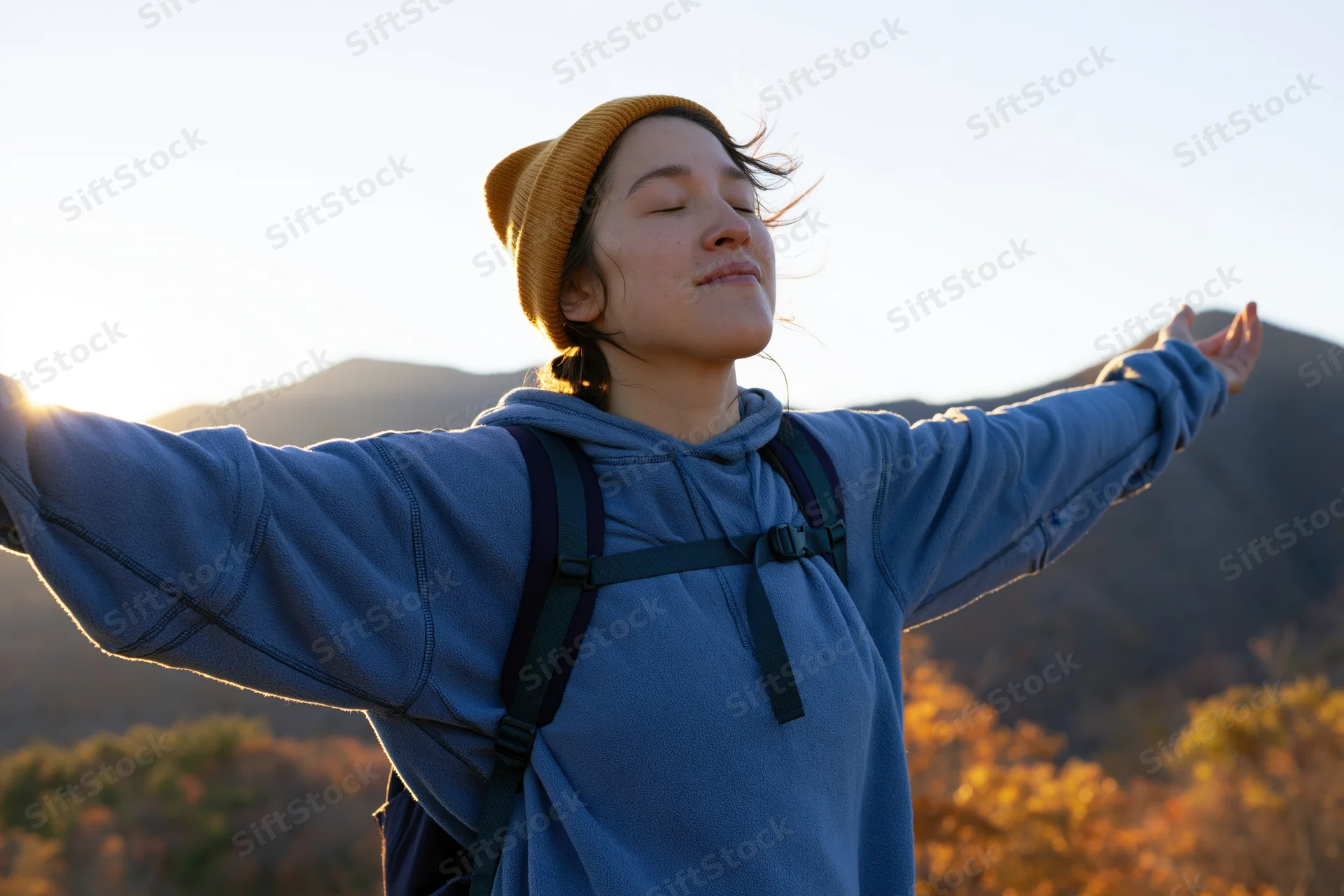Woman with arms outstretched facing sunrise in mountain landscape