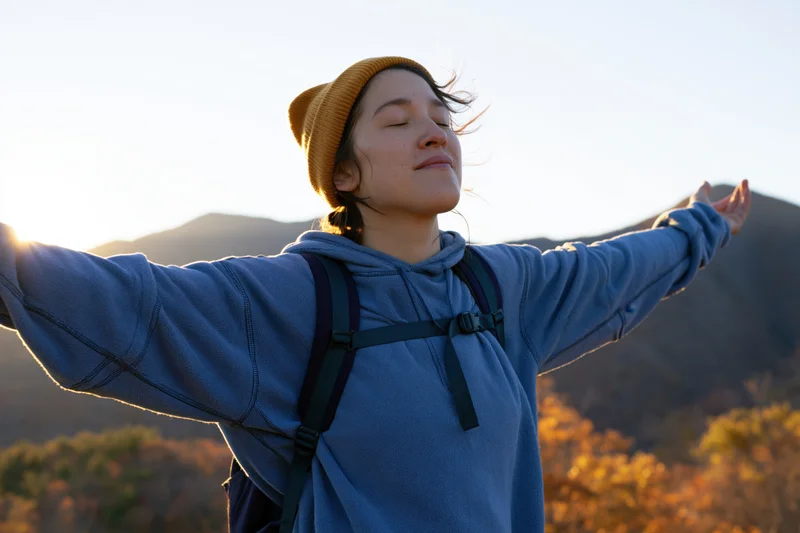 Woman with arms outstretched facing sunrise in mountain landscape