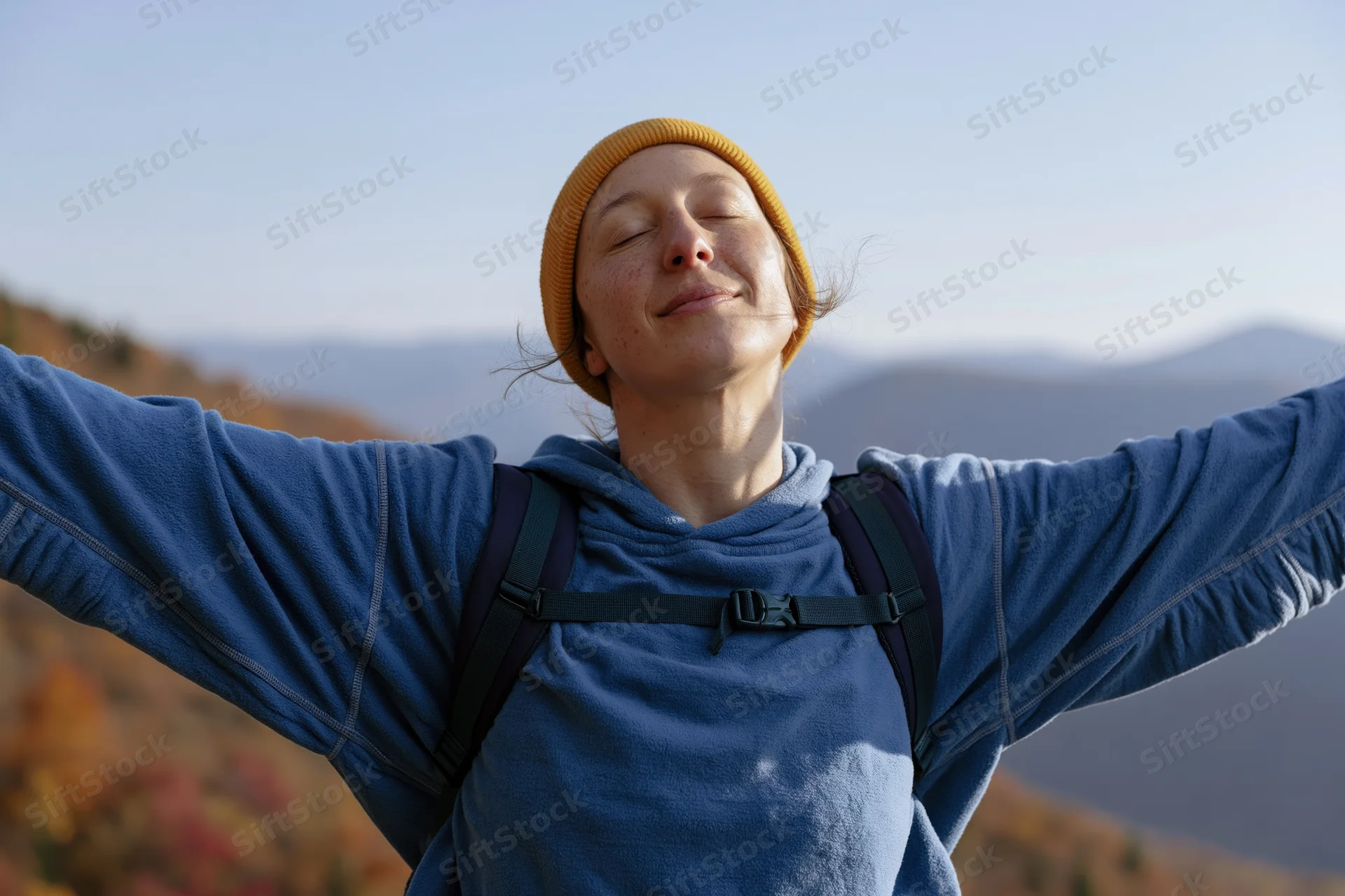 Woman with arms open and eyes closed standing on a mountain trail in autumn forest