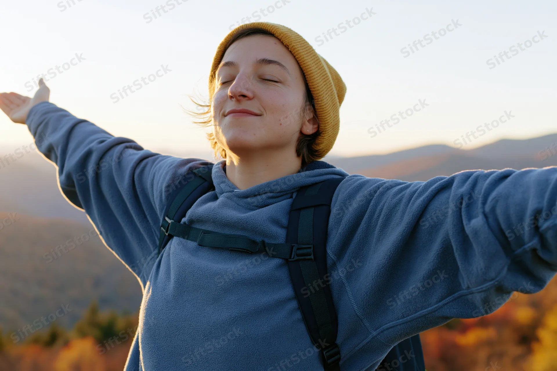 Woman with arms outstretched smiling with eyes closed in mountain landscape at sunrise