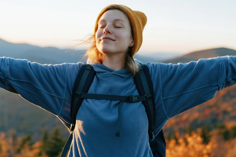 Woman with arms outstretched smiling with eyes closed in mountain landscape at sunset