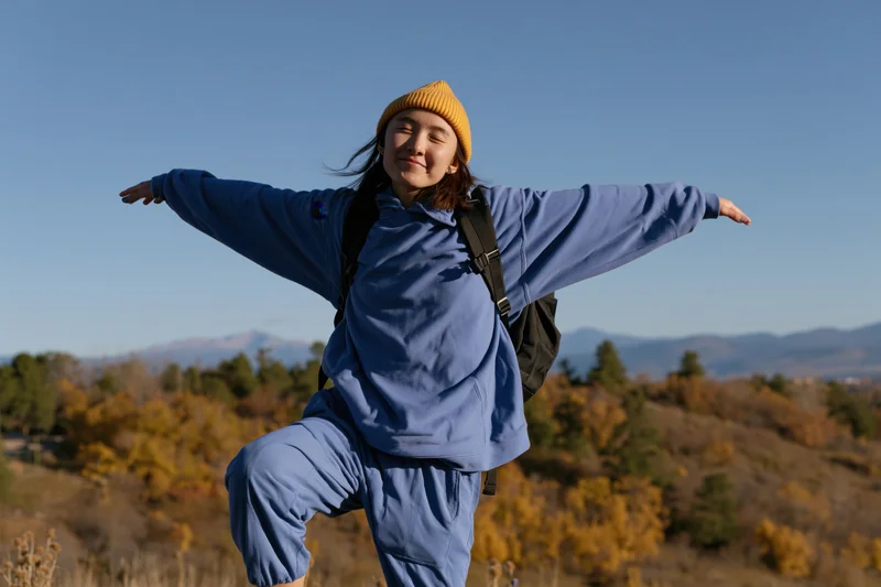 Woman smiling with arms outstretched while hiking on a hill in autumn landscape