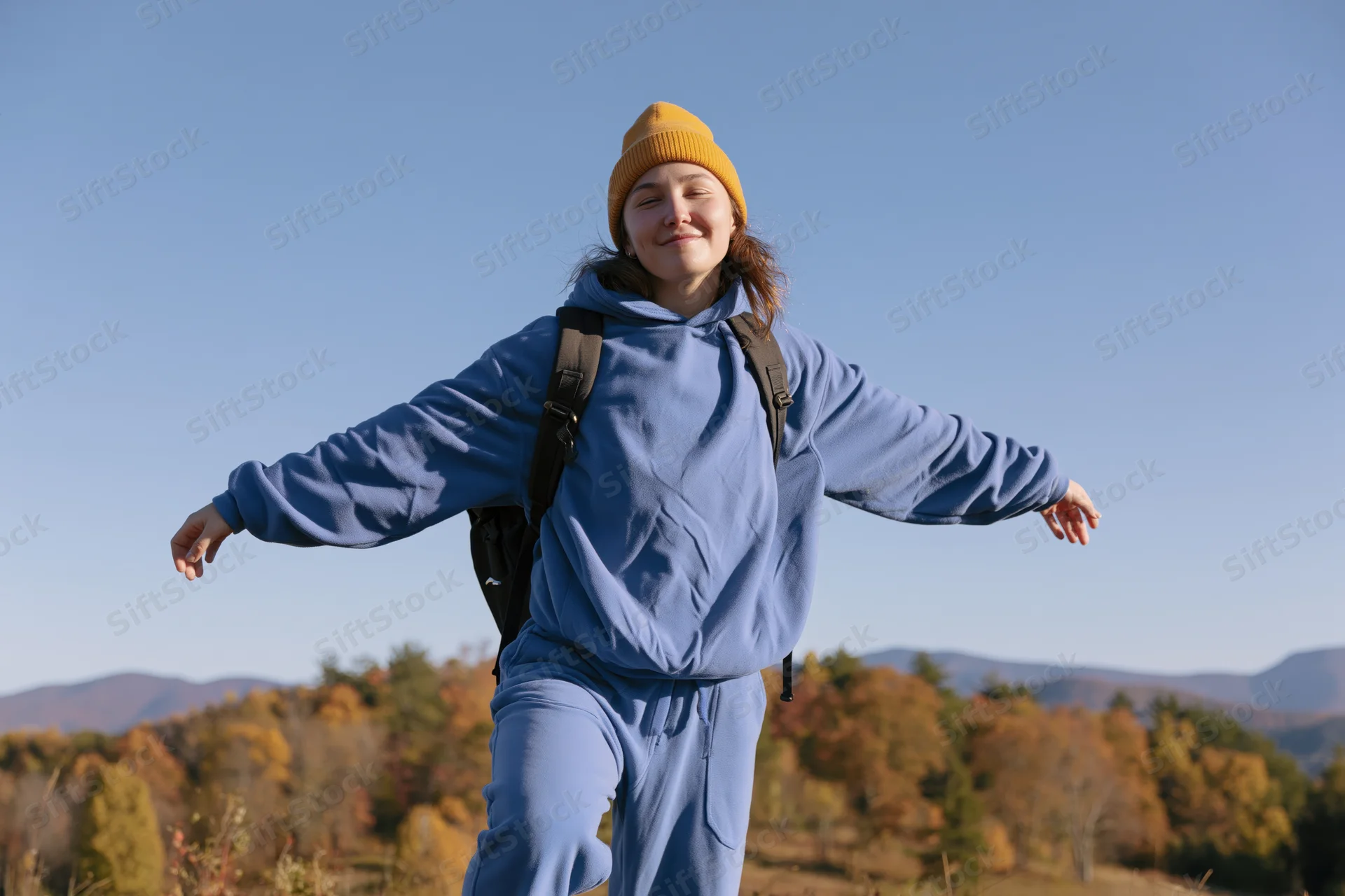 Woman hiking outdoors with arms outstretched on a hillside in autumn forest