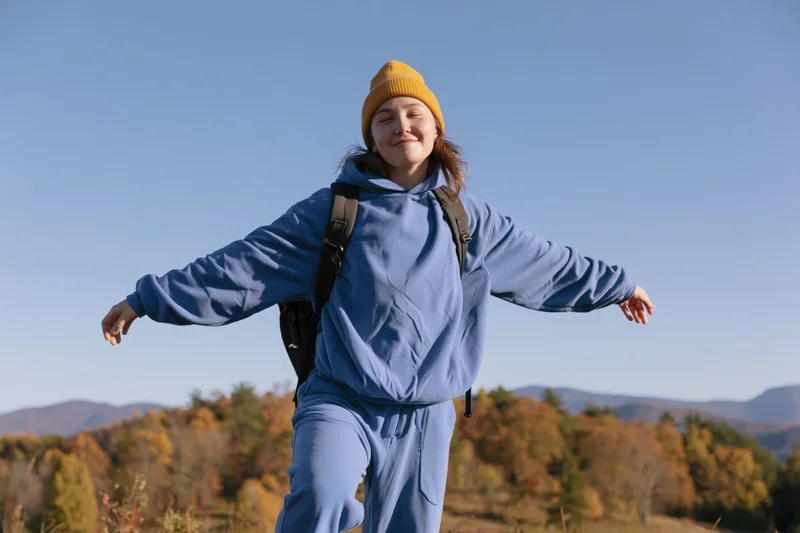 Woman hiking outdoors with arms outstretched on a hillside in autumn forest