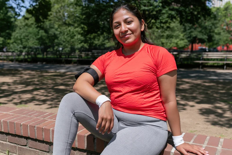 Woman in sportswear sitting on brick bench in park smiling at camera