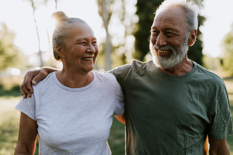 Elderly couple smiling and embracing outdoors in a park during golden hour