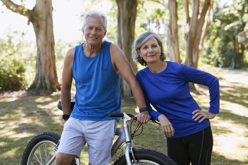 Senior couple smiling while standing with bicycle in park
