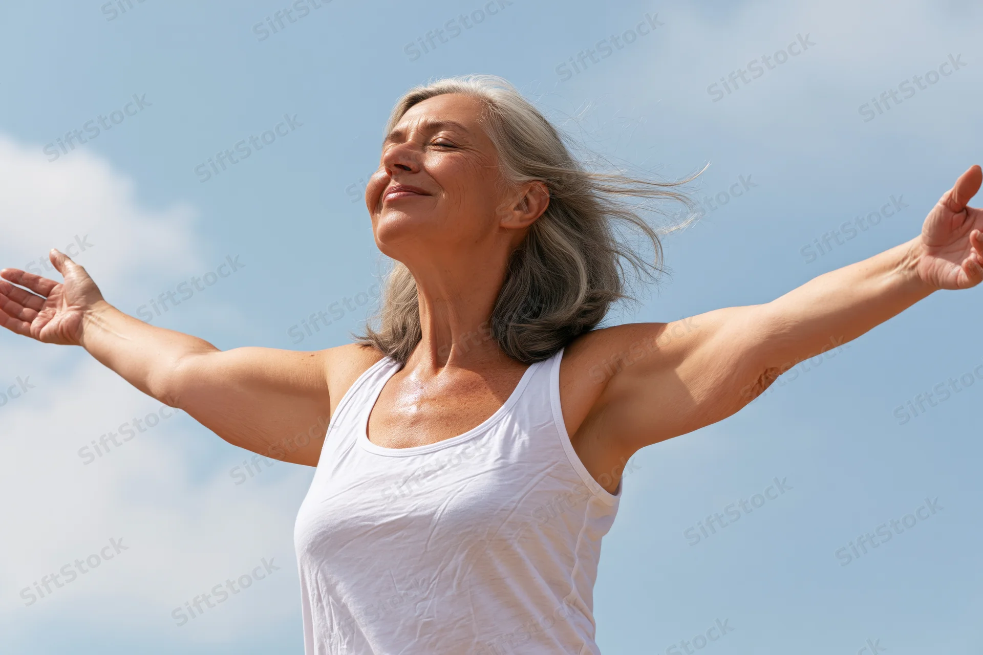 Senior woman with arms outstretched smiling under clear blue sky