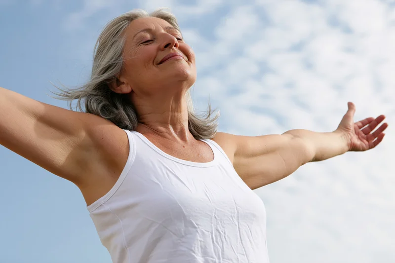 Senior woman with arms outstretched smiling against blue sky outdoors